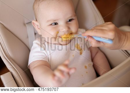 High Angle View Of Mother Feeding Cheerful Baby Boy With Porridge, Baby Sitting In High Chair All Me