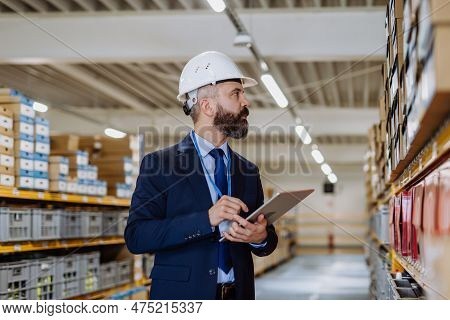 Manager In Suit Controlling Goods In A Waehouse.
