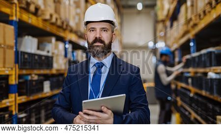 Manager In Suit Controlling Goods In A Waehouse.