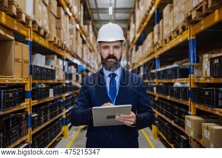 Manager In Suit Controlling Goods In A Waehouse.