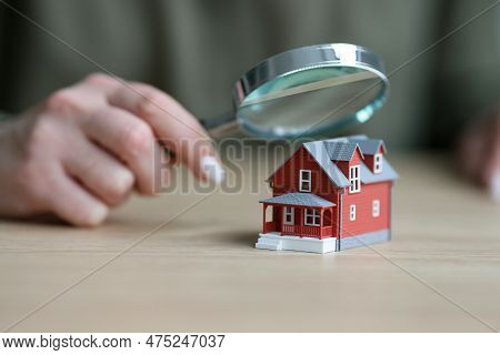 Woman Holds Magnifier Glass Above Small Model Of Townhouse. Female Realtor Checks Condition Of Real 