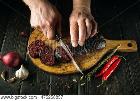Slicing Blood Sausage By The Hands Of A Cook On A Cutting Board. Cooking National Dish On The Kitche