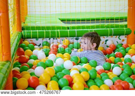 Toddler Baby Plays In The Pool With Balls. Child Boy Crawling In The Pool With Plastic Balls. Kid Ag