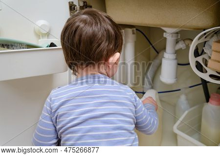 A Child Is Playing With Chemical Cleaning Products Under The Sink In The Kitchen. Baby Holds Bottles