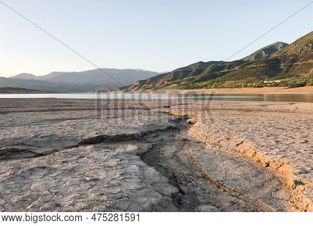 Beautiful Landscape With Setting Sun: Mountains, Lake, Cracked Earth With Stones -dried-up Riverbend