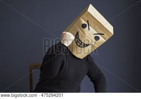 A Man In A Black Turtleneck With A Bag On His Head, With A Drawn Angry Emoticon, Shows His Fist Whil