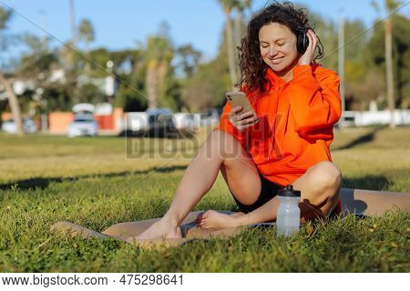 Young Smiling Sportswoman In Wirelles Headphones Listening Music And Using Cellphone During Workout 