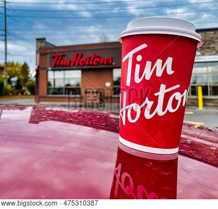 Oshawa, Canada - 19 October 2022: Cup Of Tim Hortons Coffee On Red Car In Front Of Outlet With Logo