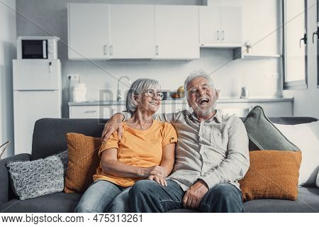 Happy Mature Husband And Wife Sit Rest On Couch At Home Hugging And Cuddling, Show Care Affection, S