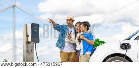 Concept Of Progressive Happy Family Enjoying Their Time At Wind Farm With Electric Vehicle. Electric