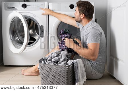 Middle Aged Single Man With Laundry Basket And Dirty Clothes Near Washing Machine At Home. Millennia