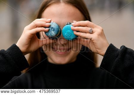 Beautiful Girl Wear In Black Keeps Two Sweet French Macaroons On Eyes