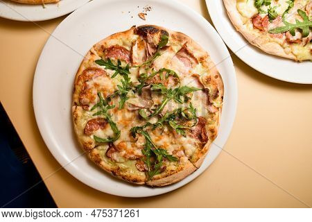 Three Ready-made Mini Pizzas With Jamon, Ruccola Covered With Cheese On Light Table
