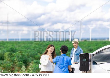 Concept Of Progressive Happy Family Enjoying Their Time At Wind Farm With Electric Vehicle. Electric