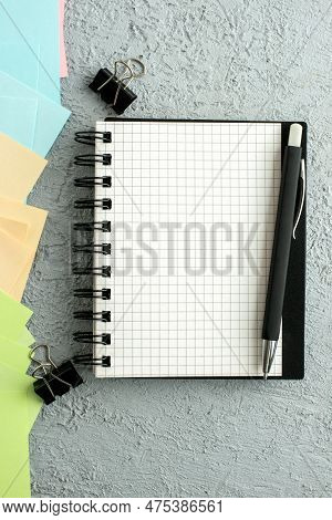 Vertical View Of Pen On Spiral Notebook On Black Book And Coloured Envelopes On Gray Distressed Back
