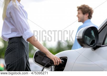 Focus Hand Insert Ev Charger To Electric Vehicle At Public Charging Point In Car Park With Blur Busi