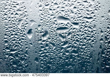 Backlit Chaotic Water Drops On Lightbeige And Blue Glass Background. Condensation After Rain Or Show