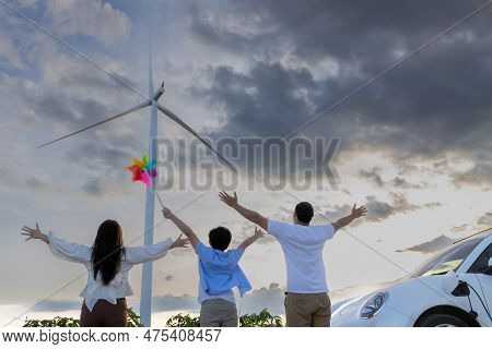 Concept Of Progressive Happy Family Enjoying Their Time At Wind Farm With Electric Vehicle. Electric