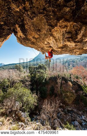 Girl Climber On An Overhanging Rock. A Sports Woman Climbs A Rock Against The Backdrop Of Mountains.