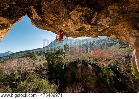Girl Climber On An Overhanging Rock. A Sports Woman Climbs A Rock Against The Backdrop Of Mountains.