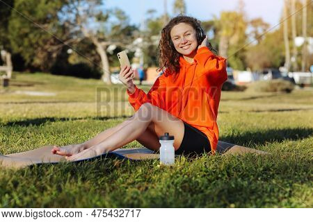 Young Smiling Sportswoman In Wirelles Headphones Listening Music And Using Cellphone During Workout 