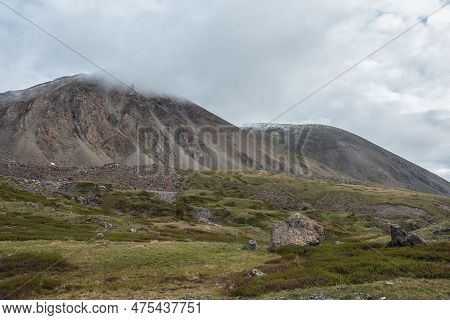 Dramatic Landscape With Big Stones On Hills Against High Mountain With Sharp Rocks In Rainy Low Clou