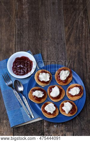 A Flat, Top View Of A Pikelets/pancakes/battercakes With Strawberry Jam And Whipped Cream On A Blue 