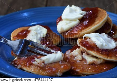 A Close-up Of A Fork Cutting Into A Messy Plateful Of Pikelets/pancakes/battercakes To Illustrate An