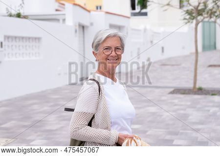 Portrait Of Beautiful Happy Woman Traveler Walking In A City Street Holding Backpack. Smiling Elderl