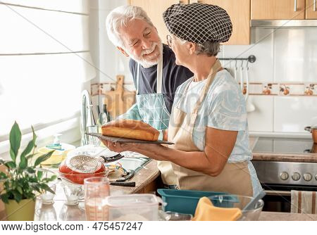Proud Senior Woman Holding Her Freshly Baked Homemade Plumcake At Her Husband Which Is Washing The D
