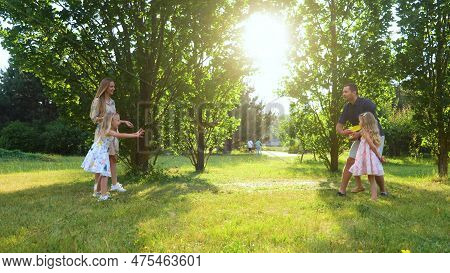 Positive Family Throwing Frisbee Disk In Park. Smiling Girl Catching Frisbee Plate. Young Parents Pl