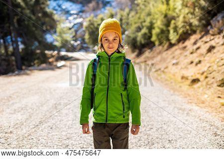 Boy With A Backpack In The Forest. The Child Is Standing In The Middle Of The Road In The Forest. Hi