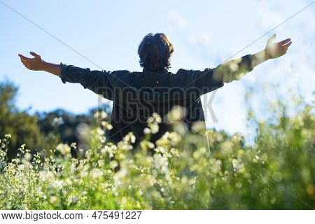 Back View Of Man Outstretching Arms In A Green Field. Travel Destination Tourism. Outdoor Leisure Ac
