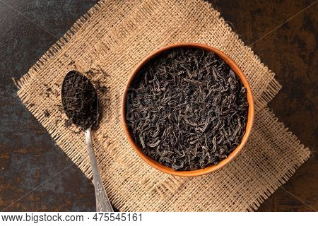 Dry Black Tea Leaves In A Clay Bowl And A Vintage Spoon On A Dark Wooden Background Top View. Large-