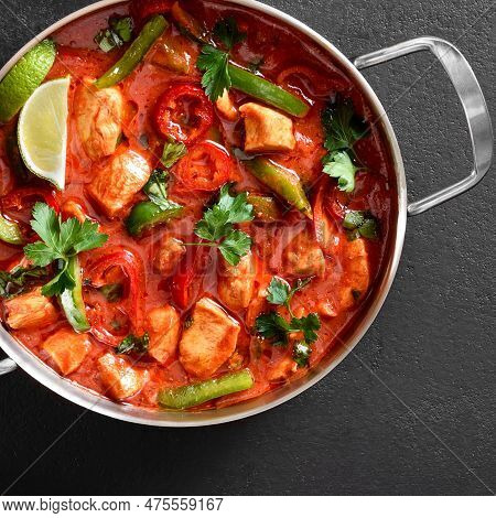 Close Up View Of Thai Style Red Chicken Curry With Vegetables In Pan Over Black Stone Background. To