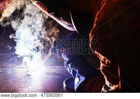 A Welder In A Welding Mask And Gloves Welds With Electric Arc Welding Using Electrodes On Metal.