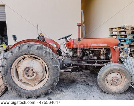 Small Old Red Metal Minitractor Stands Against The Wall Of A Building