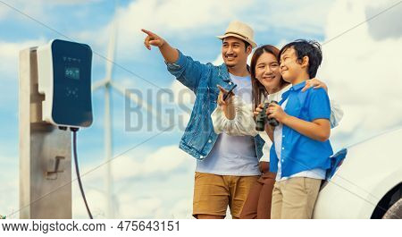 Concept Of Progressive Happy Family Enjoying Their Time At Wind Farm With Electric Vehicle. Electric