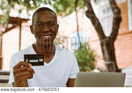 Happy Afro American Man With Glasses Sitting At Table In Cafe With Cup Of Coffee And Laptop On Summe