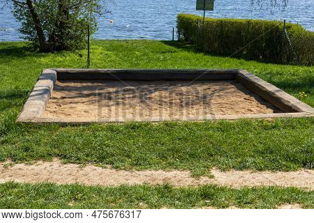 A Square Sandpit For Children In A Meadow By The Water