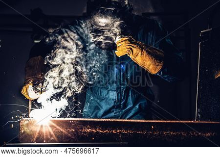 Metal Welder Working With Arc Welding Machine To Weld Steel At Factory While Wearing Safety Equipmen