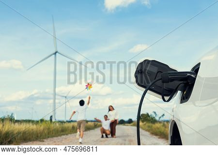 Concept Of Progressive Happy Family Holding Windmill Toy And Relax At Wind Farm With Electric Vehicl