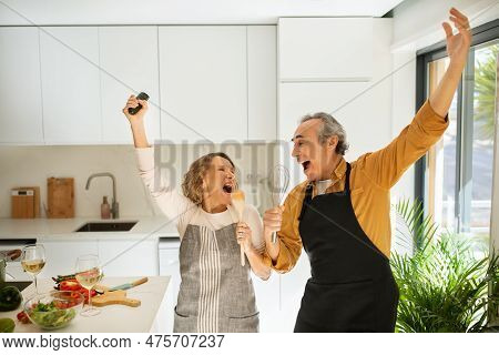 Joyful Senior Spouses Having Fun While Cooking Together At Home, Singing Songs And Dancing At Kitche