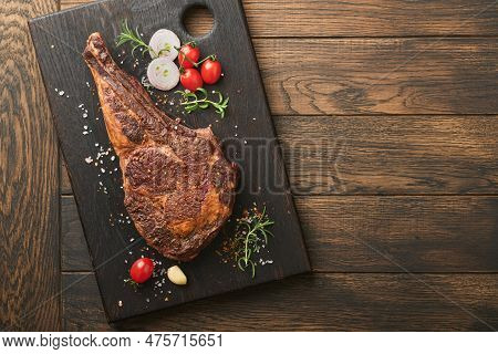Tomahawk Steak. Sliced Grilled Tomahawk Beef Steak With Baked Cherry Tomatoes, Herbs And Salt On Old