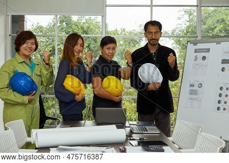 Four Of Engineer Secretary And Chief Standing Holding Safety Helmet And Fist Up In Constrcution Site
