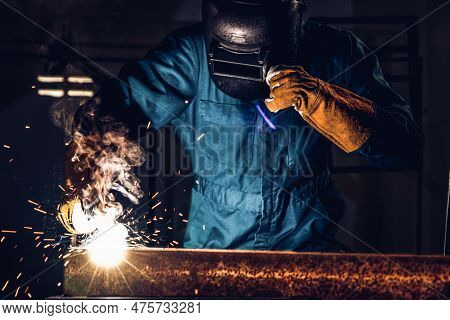 Metal Welder Working With Arc Welding Machine To Weld Steel At Factory While Wearing Safety Equipmen