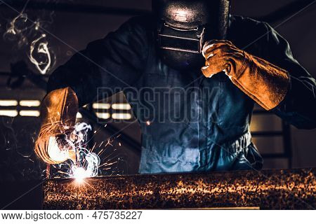 Metal Welder Working With Arc Welding Machine To Weld Steel At Factory While Wearing Safety Equipmen