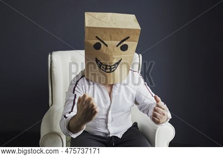 A Man With A Paper Bag On His Head, With An Evil Smiley Face Drawn, Sits On A White Chair, Gloats Em