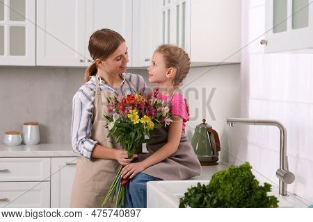 Little Daughter Congratulating Mom With Bouquet Of Flowers In Kitchen. Happy Mother's Day