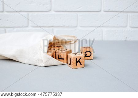 Wooden Cubes With Black Letters Poured Out Of A Cloth Bag On A Gray Table. Front View